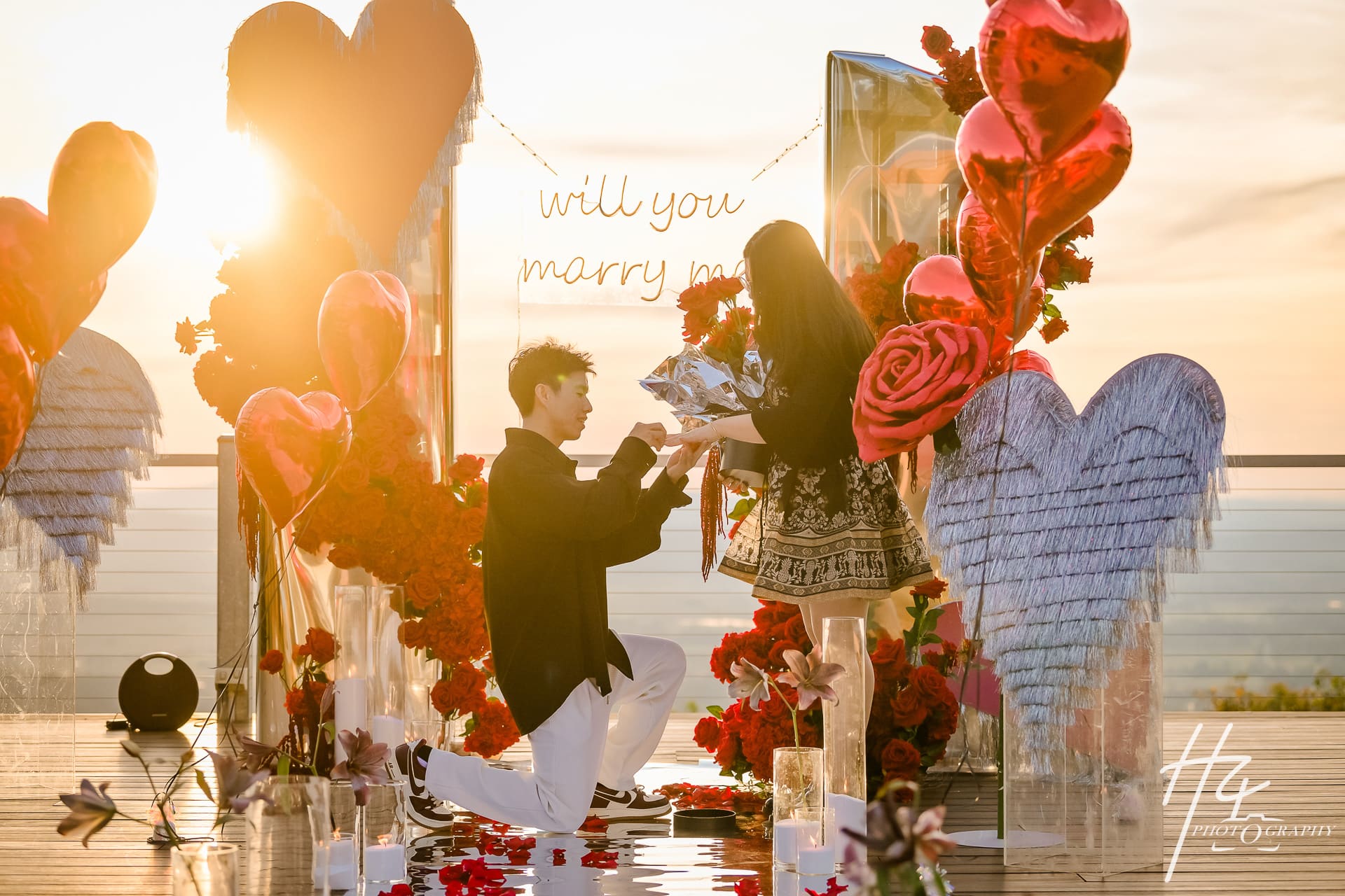 A proposal at sunset among red florals and heart installations