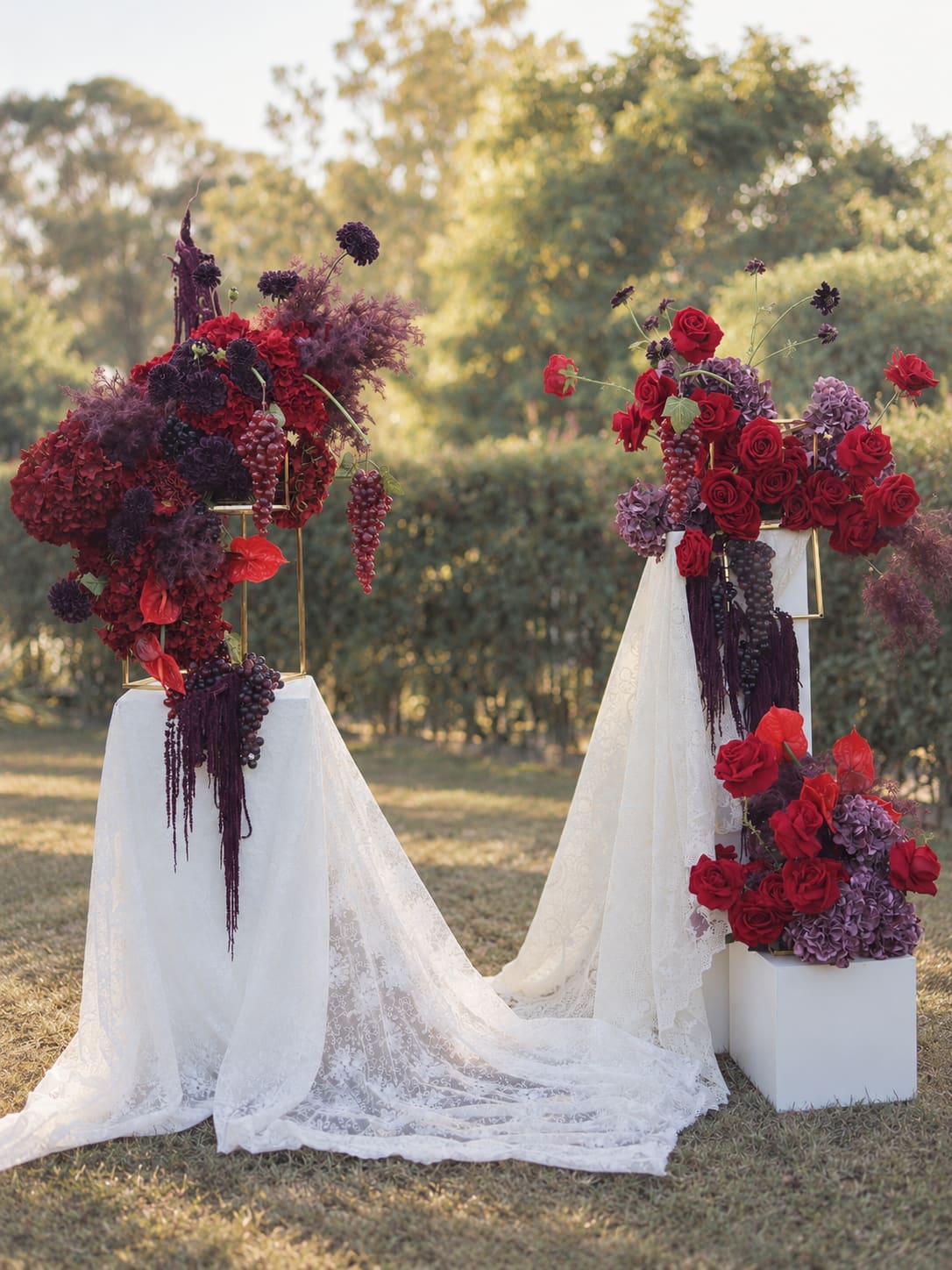 Front view of Bordeaux Garden red and burgundy florals with white lace draping and three plinths