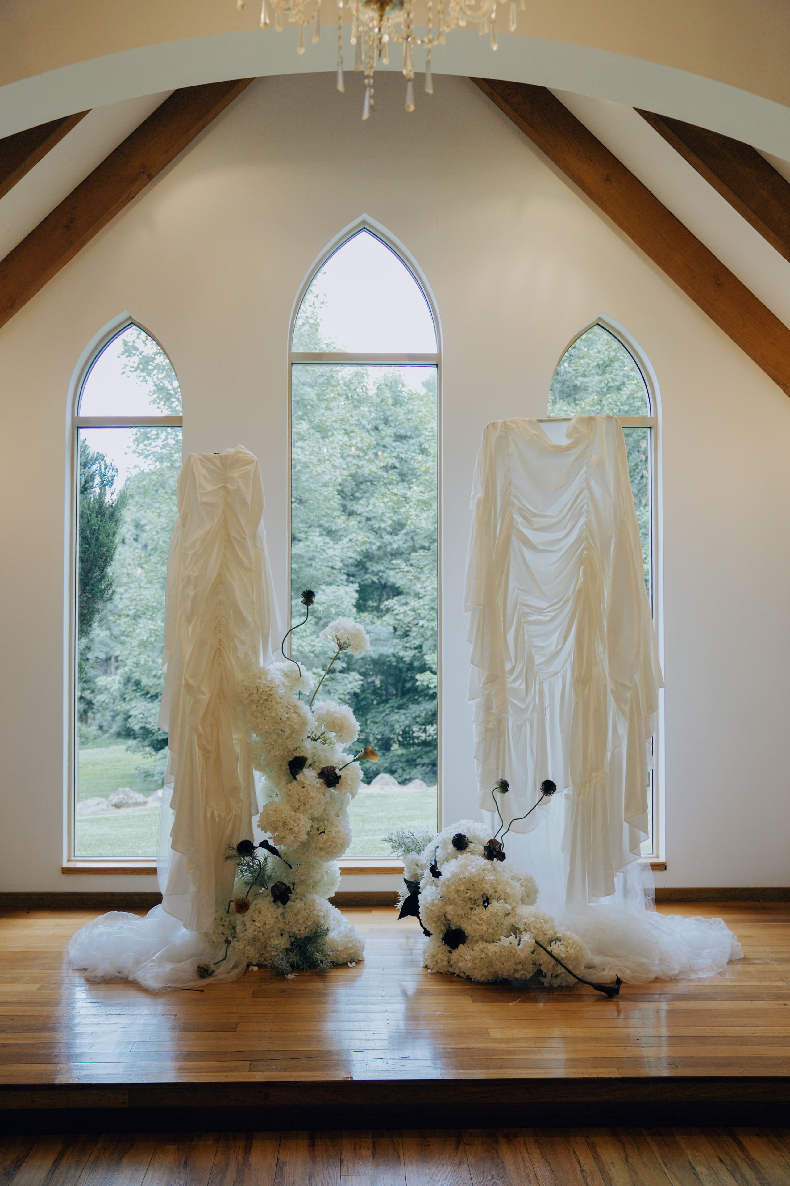Two draped white columns with sculptural white florals in a chapel with arched windows