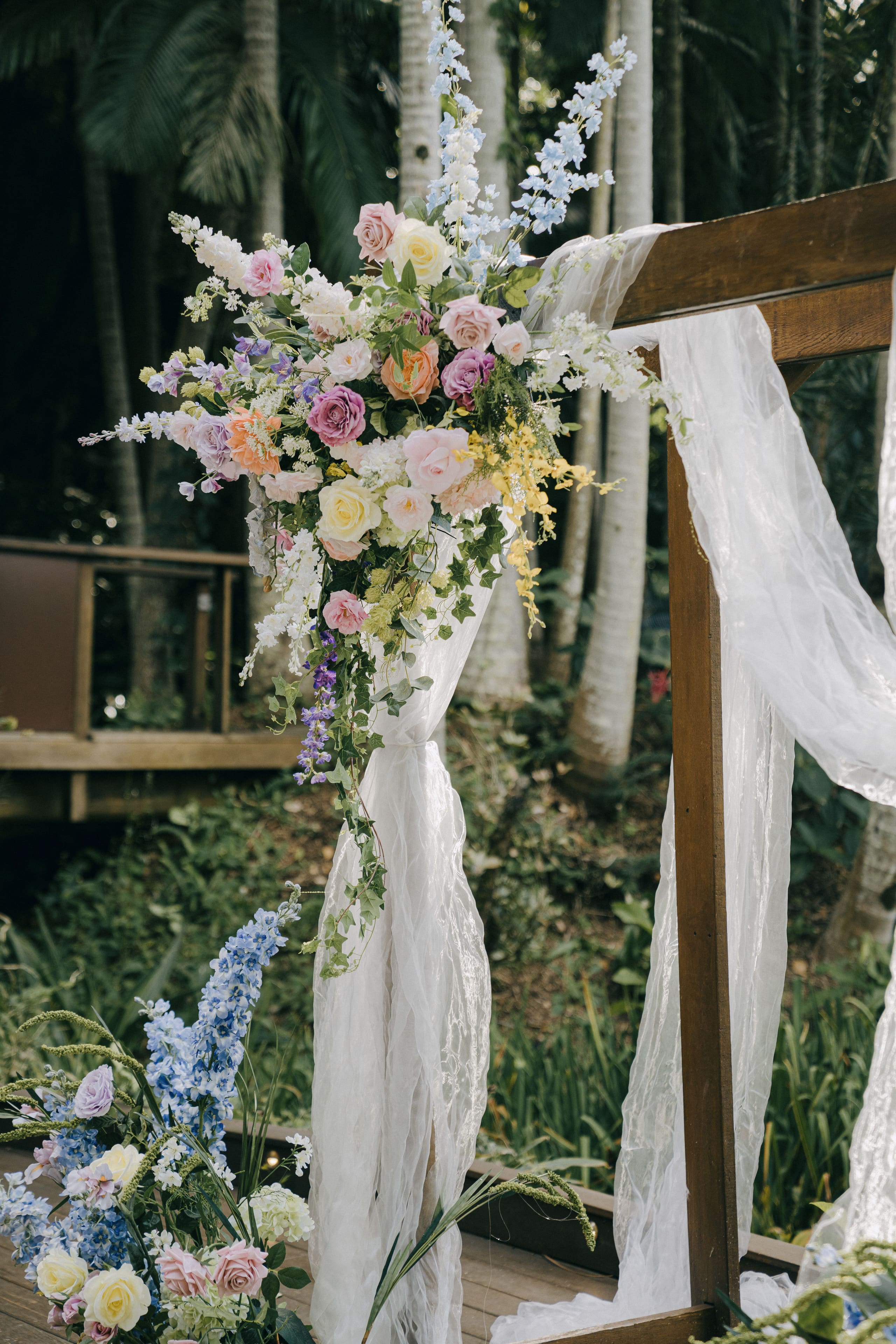 A ceremony arch dressed in pastel florals and sheer draping in a garden setting