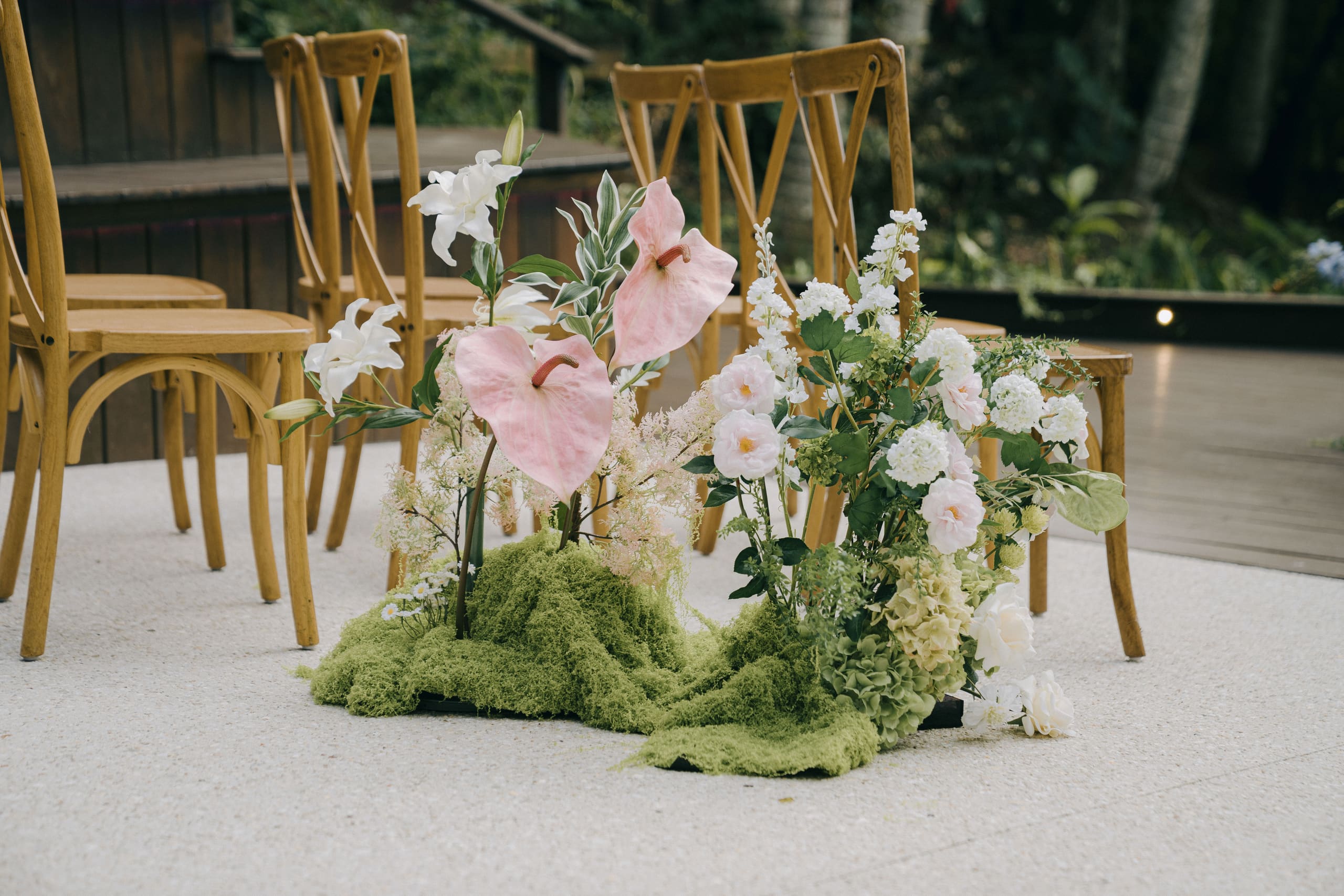 Pink anthurium, white blooms and moss at the foot of the ceremony chairs