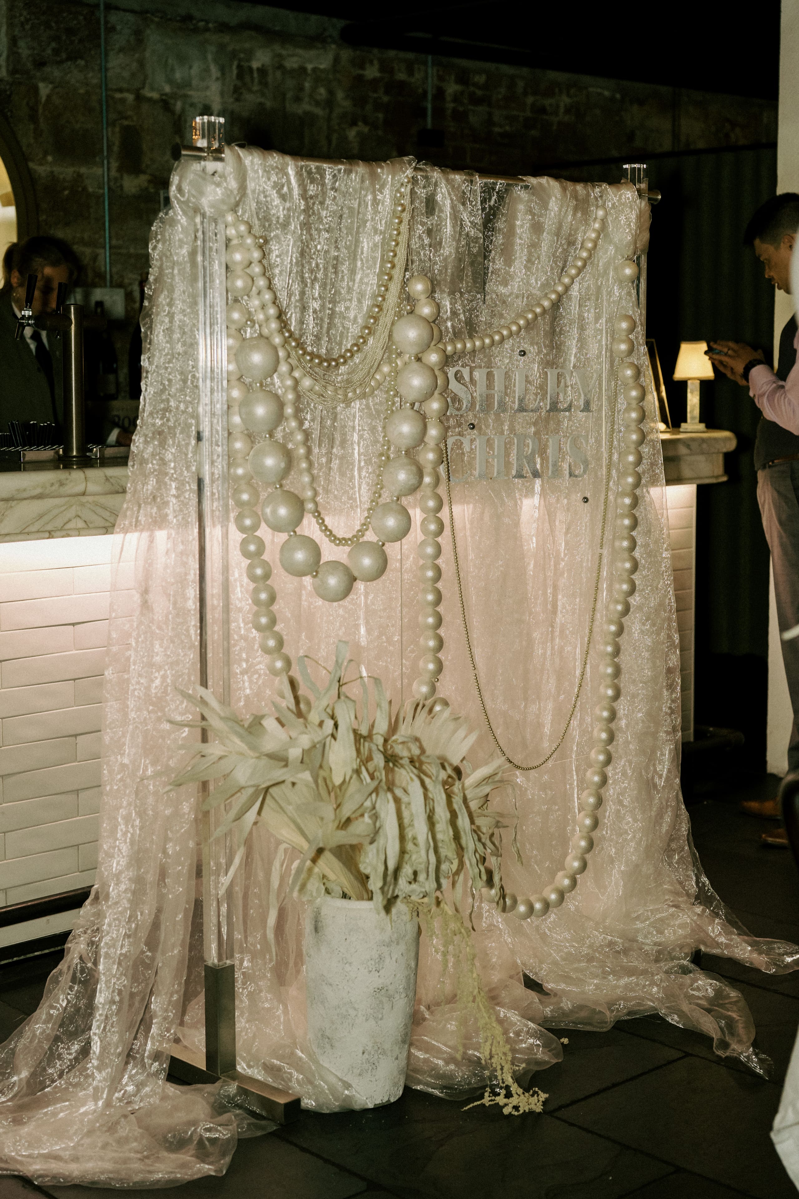 Oversized pearl strands draped over sheer fabric with dried palm