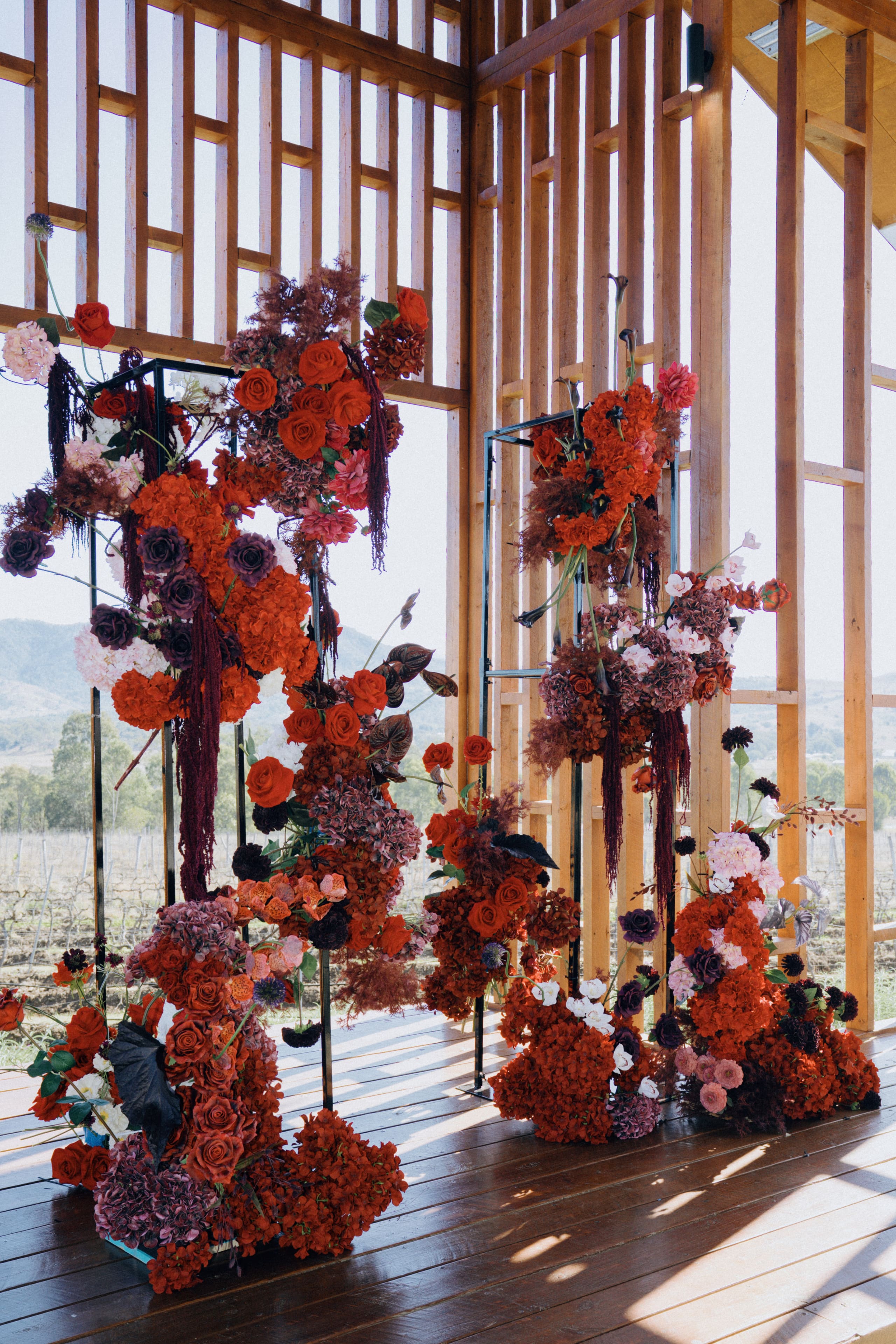 Deep red and plum floral installations framing a timber pavilion