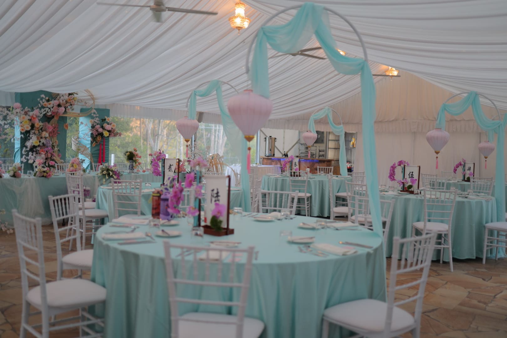 Reception marquee with teal linen, draped fabric and pink lanterns