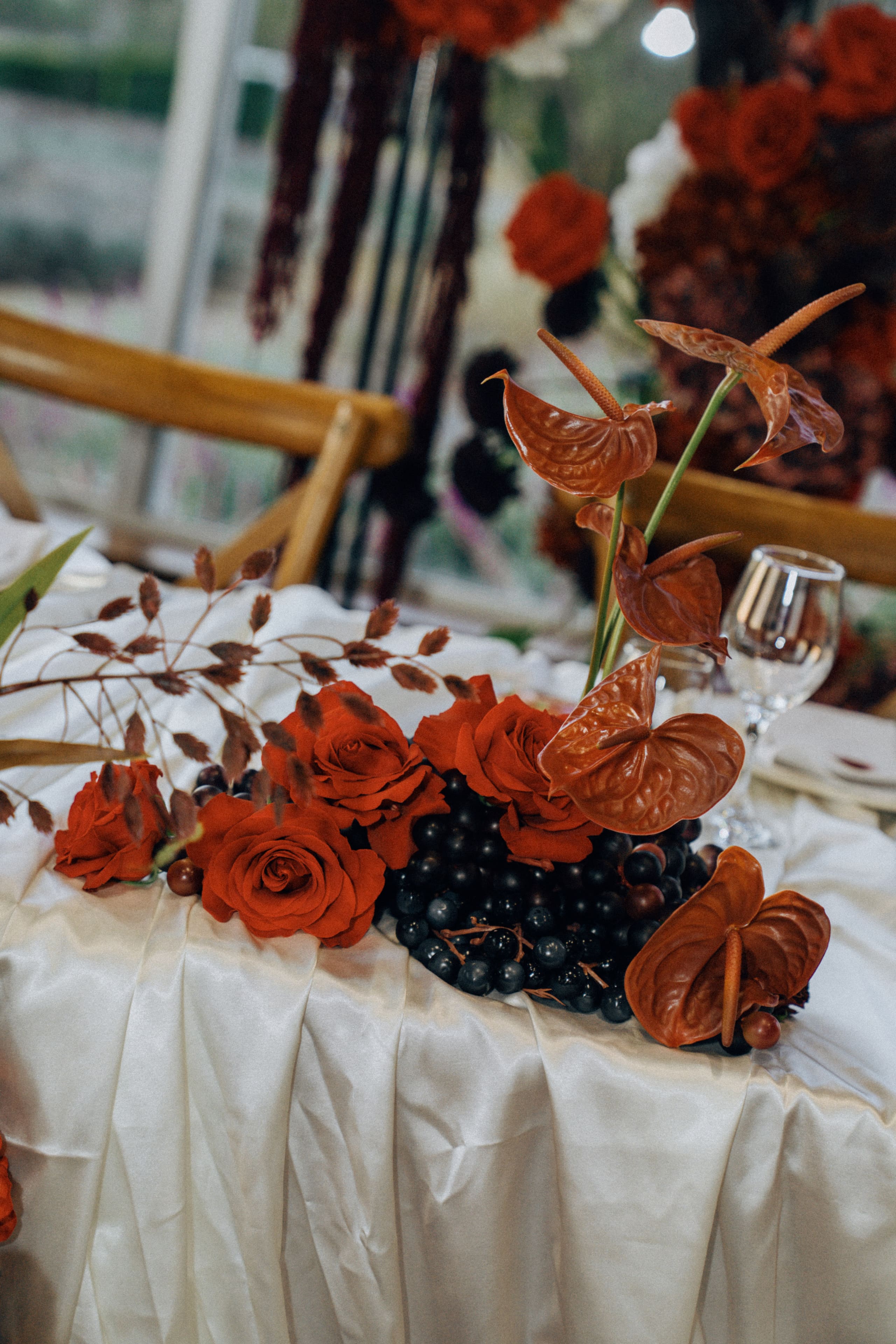Table centrepiece of red blooms and dark grapes on ivory satin